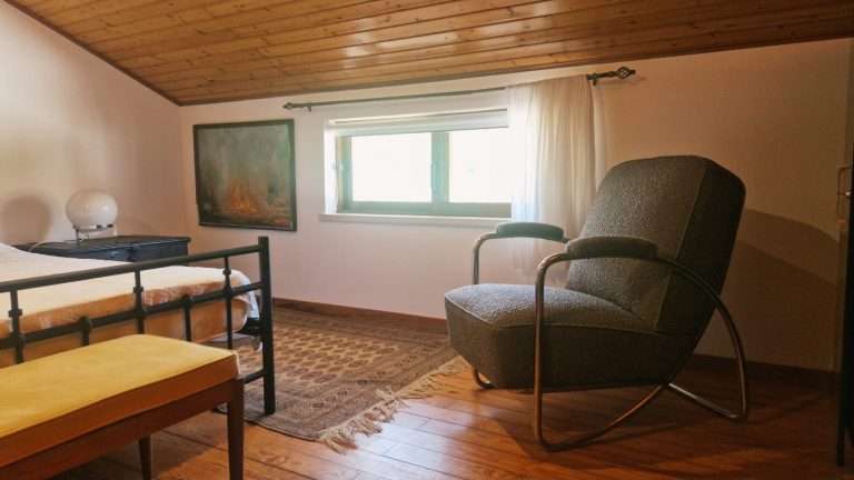 Quarto com camas de ferro, poltrona e luz natural