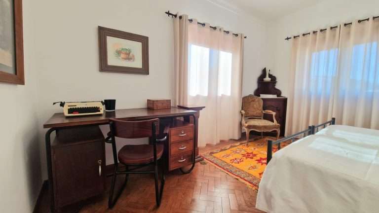 Quarto com camas individuais, secretária e janelas com cortinas